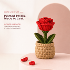 A crocheted 3D-printed rose planter with a red flower, green stem and leaves, and a beige woven pot, displayed on a light pink surface with a soft pink background and text on the left.