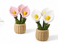 Two crocheted calla lily plant arrangements in beige woven pots, one with pink flowers and one with white flowers, both with yellow centers and green stems, on a white background.