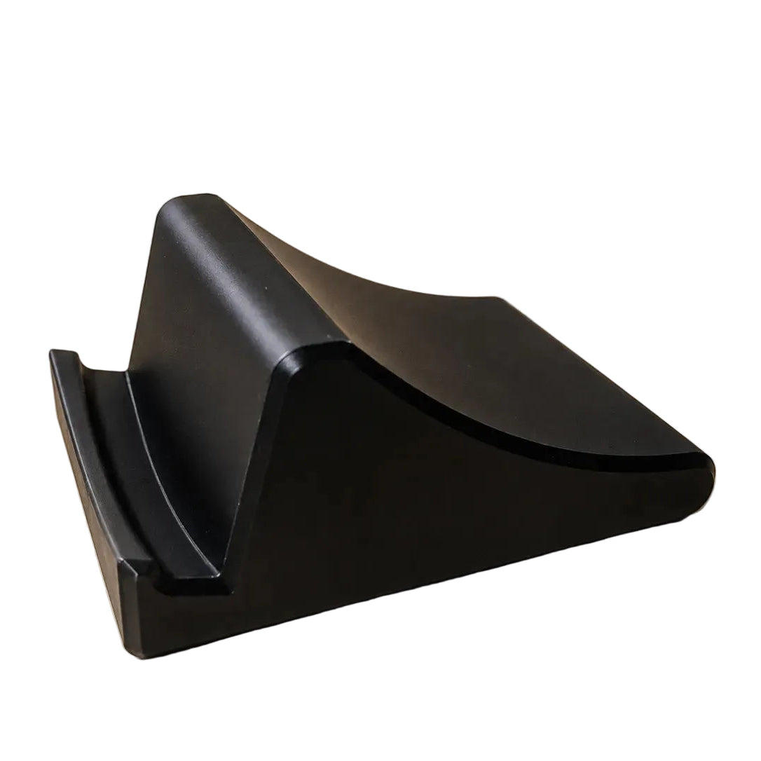 A matte black curved triangular stand or cradle photographed on a plain warm beige studio background.
