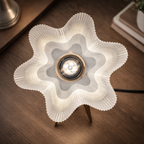 A star-shaped table lamp with a pleated white shade and a warm glowing light bulb in the center, set on a dark wooden tabletop.